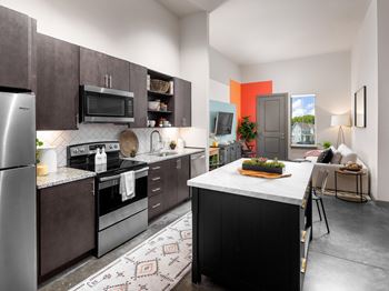 A kitchen with a refrigerator, microwave, oven, and sink.